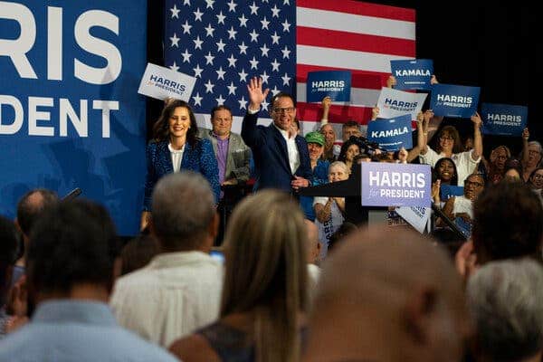 Gretchen Whitmer, left, and Josh Shapiro, stand on a stage with a group of supporters behind them, some of them waving Harris for President signs.