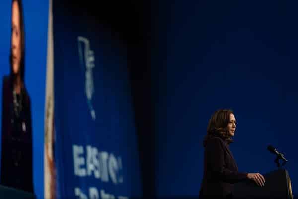 Vice President Kamala Harris speaking in Houston this month. She is standing at a podium, and a large photo of her is projected on the wall behind her. 